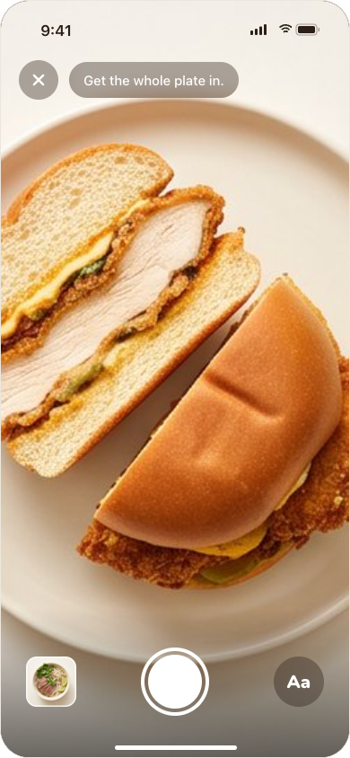 Donbu's camera framing a chicken sandwich on a plate, with the hint: get the whole plate in. The shutter sits between a button for picking a photo and the Aa button for typing.